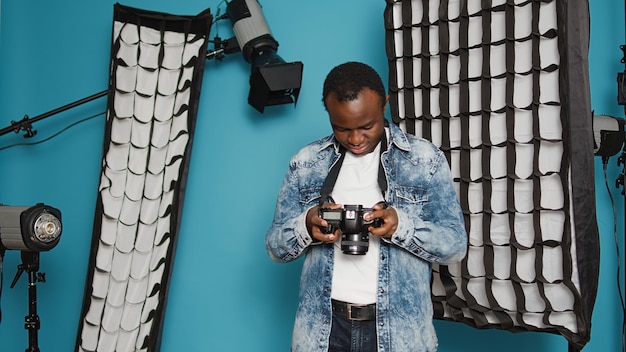 Free photo photographer looking at dslr camera to check image in studio, taking pictures with photography equipment and lighting. male model using focus lens, backstage lights and tools as hobby.