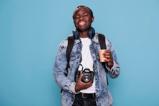 Free photo photography enthusiast with dslr device and journey rucksack getting ready for vacation journey. smiling heartily young man having trip backpack and professional camera going on weekend holiday.