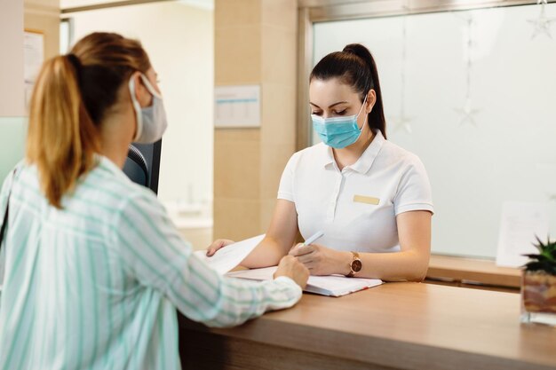 Physical therapist with face mask writing data of her client at reception desk