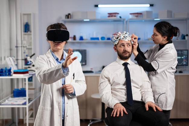 Free photo physician doctor with virtual reality headset while neurologist woman adjusting eeg scanner of man patient analyzing brain evolution during neurology experiment. scientist engineer using high tech