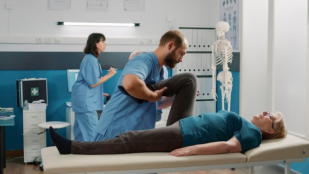 Free photo physician doing legs raise exercise to stretch legs for old patient with mechanical disorders in rehabilitation cabinet. osteopathy specialist doing physical therapy procedure to cure woman.