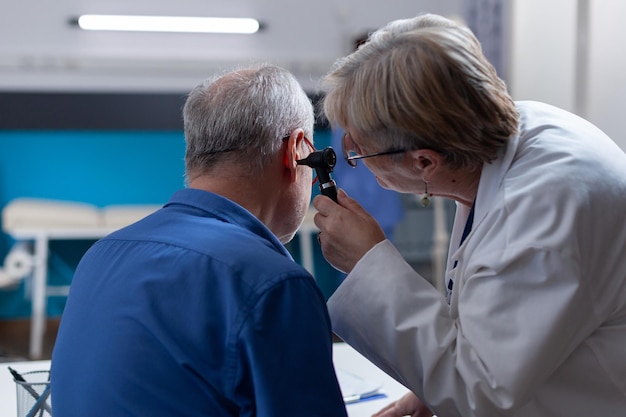 Free photo physician holding otoscope to do ear consultation for patient at checkup visit. woman doctor using otology instrument to examine infection and give medical advice to senior man.