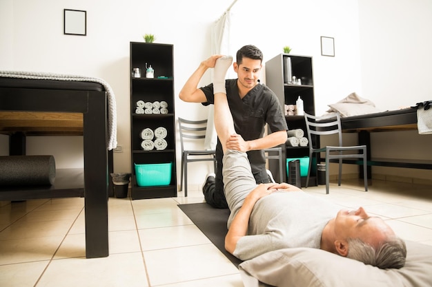 Free photo physiotherapy doctor assisting elderly patient with leg exercise in clinic