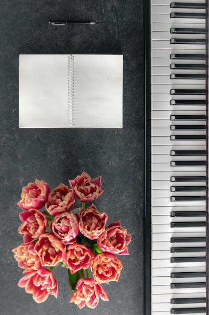 Free photo piano bouquet of tulip flowers and notepad on a dark background top view