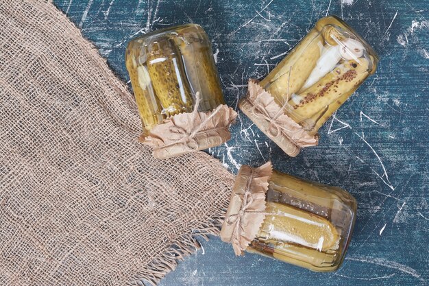 Pickled cucumbers in glass jars on blue. 