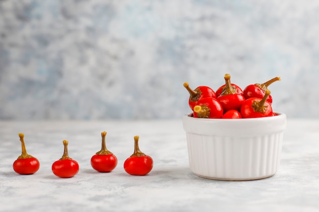 Free photo pickled small round red hot cherry chili peppers on grey concrete