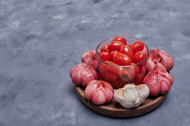 Pickled tomatoes and garlic on wooden plate.