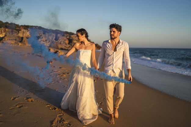 Free Photo picture of a beautiful couple posing with a blue smoke bomb in the beach