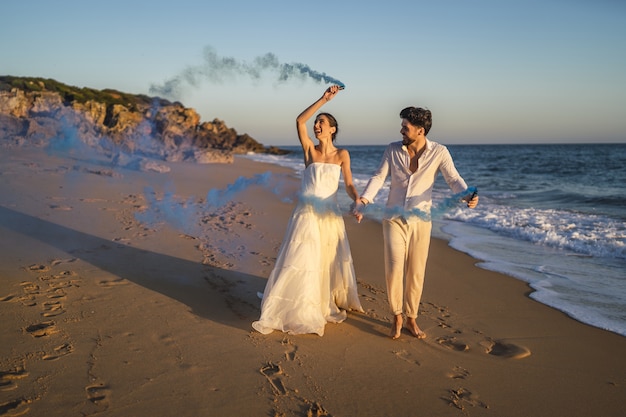 Picture of a beautiful couple posing with a blue smoke bomb in the beach