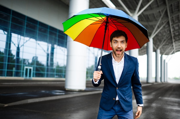 Picture of cheerful young businessman holding motley umbrella in the street