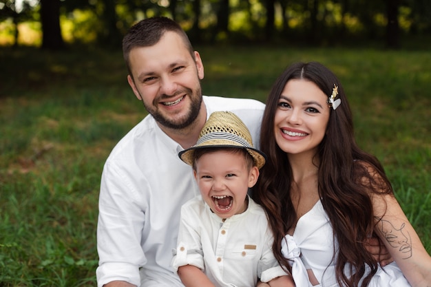 Picture of cheerful young caucasian female and male holds their child on hands, smiles and rejoices