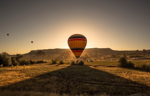 Picture of a colorful hot air balloon in a field surrounded by greenery and mountains during sunset