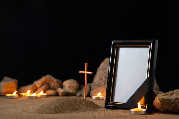 Picture frame with stones candles and little grave on dark surface