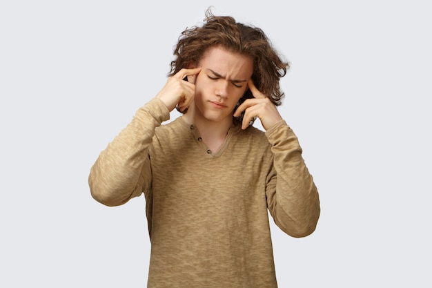 Free photo picture of frustrated stressed sick young caucasian guy feeling depressed because of terrible headache, frowning, keeping eyes closed and pressing fingers on his temples, trying to soothe pain