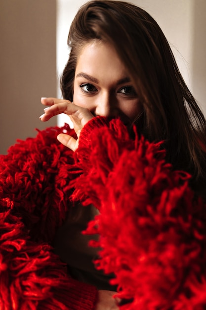 Free photo picture of lady in red jacket covering her face with her hand. woman with brown eyes looking at camera.