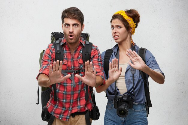 Picture of stylish young European male and female tourists, travelers or adventures looking frustrated and worried, showing stop gesture with hands, trying to settle down conflict while traveling