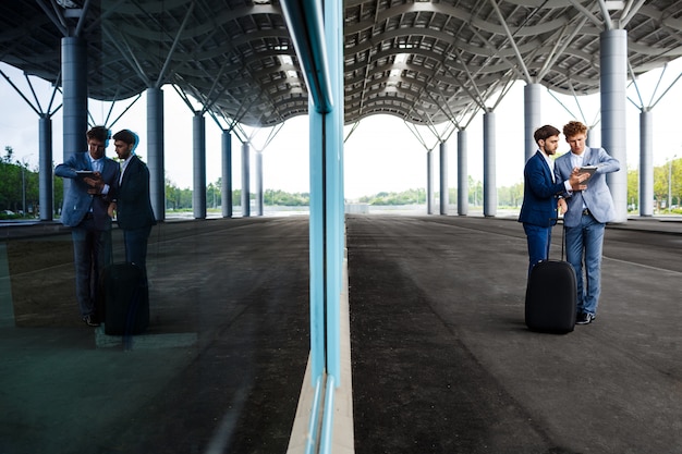 Free photo picture of  two young businessmen talking on station   and holding tablet reflected in window