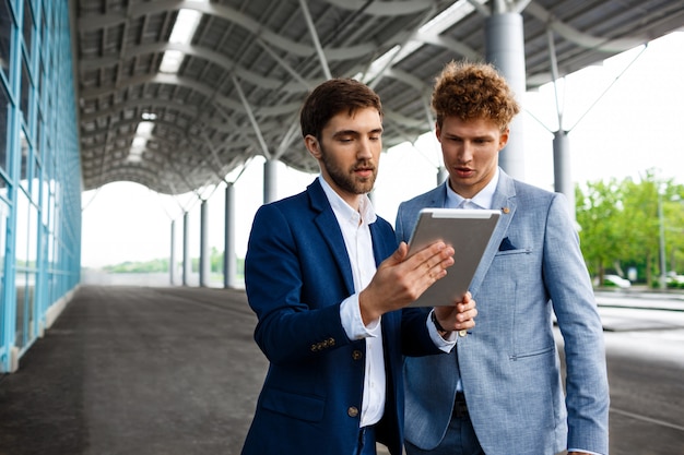 Picture of  two young businessmen talking on station  and holding tablet