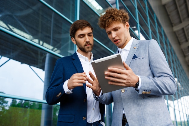 Picture of  two young businessmen talking on station   and holding tablet