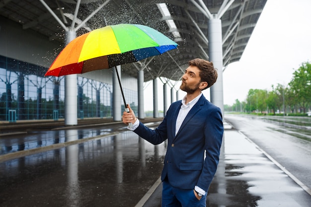 Free Photo picture of  young businessman holding colorful umbrella with sprinkles around in rainy street