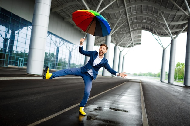 Free Photo picture of young businessman holding motley umbrella jumping and having fun at station