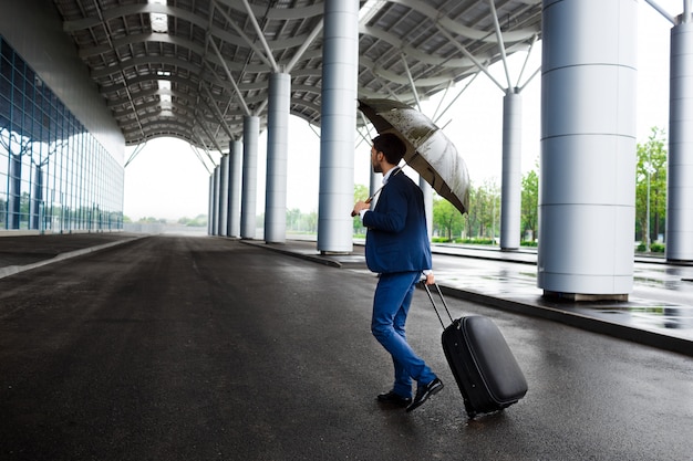 Picture of  young  businessman holding  suitcase and umbrella at rainy terminal