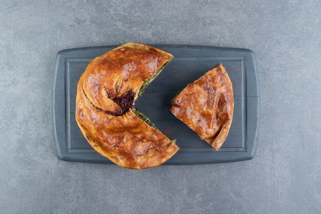 Pie stuffed with greens on black cutting board. 