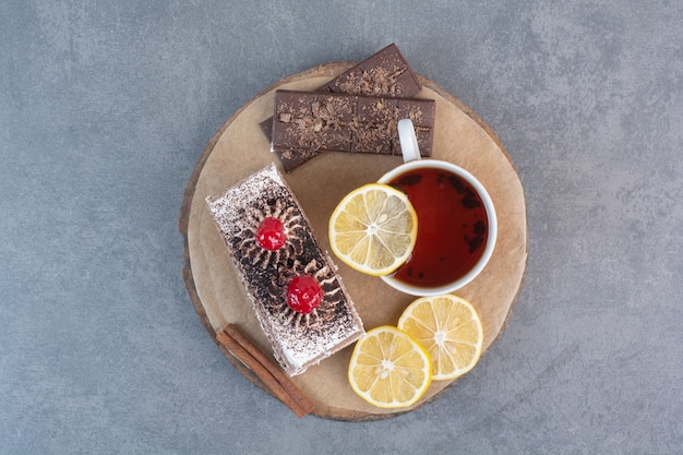 A piece of cake with sliced lemon and cinnamon stick on wooden board.