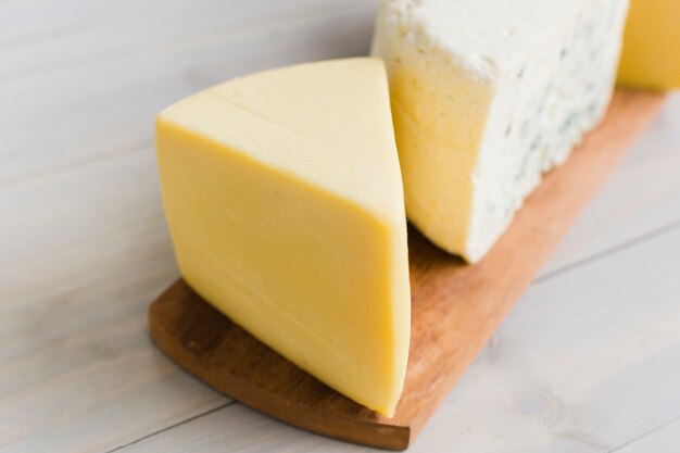 A piece of cheese on chopping board over the wooden table