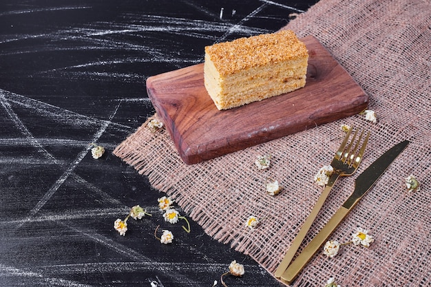 A piece of homemade honey cake on wooden board next to golden cutlery. 