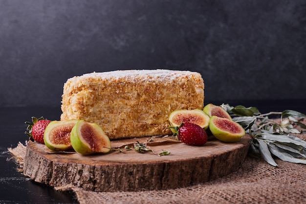 A piece of napoelon cake on dark background with figs and strawberries. 