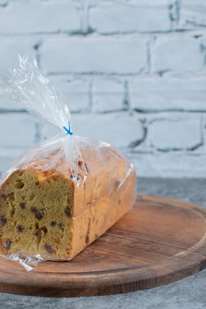 A piece of pie wrapped with plastic film on wooden board.