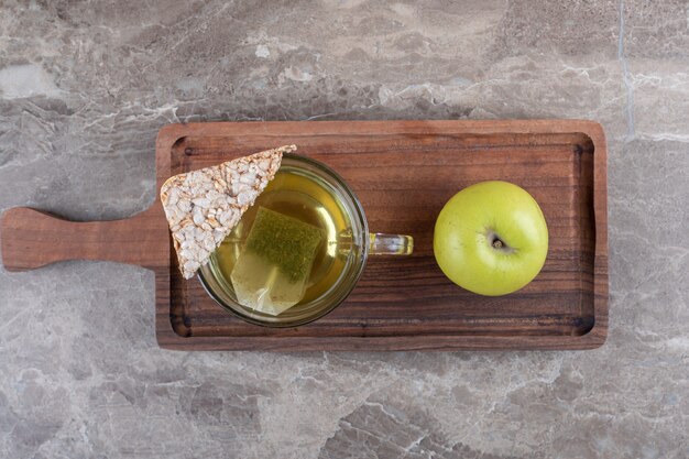 A piece of puffed rice cake, tea and apple , on the wooden tray, on the marble background.