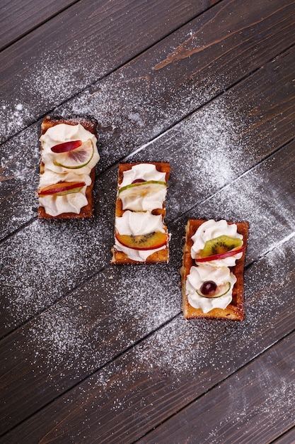 Pieces of cake with fruits covered with sugar powder served on a wooden table