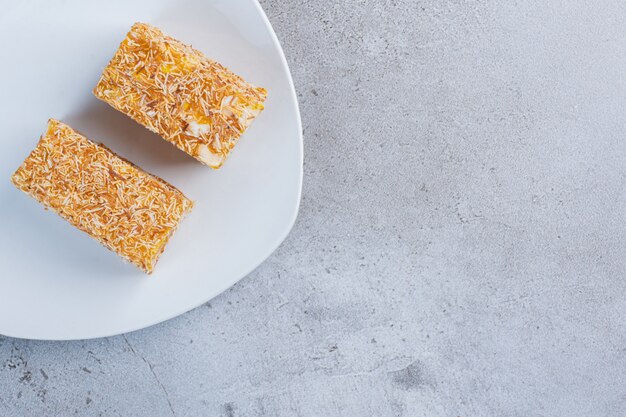 Pieces of Turkish delights coated with sprinkled candy on a white platter on marble background.