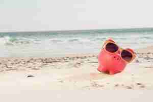 Free photo piggy bank with sunglasses kept on sand