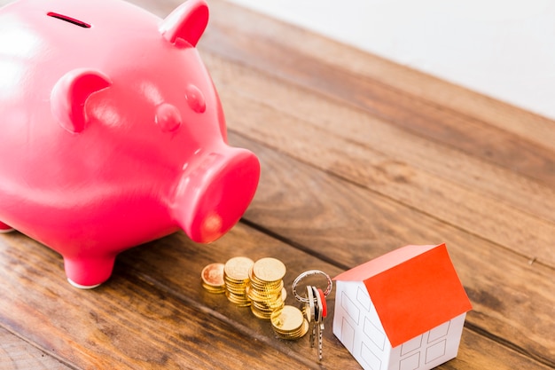 Piggybank, stacked coins, house and key on wooden desk