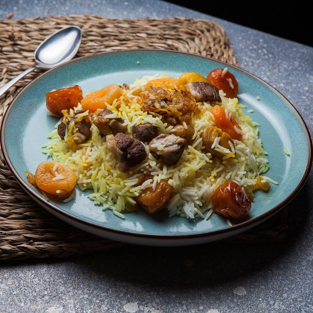 pilaf with meet and dried fruits and chestnut and spoon in round plate