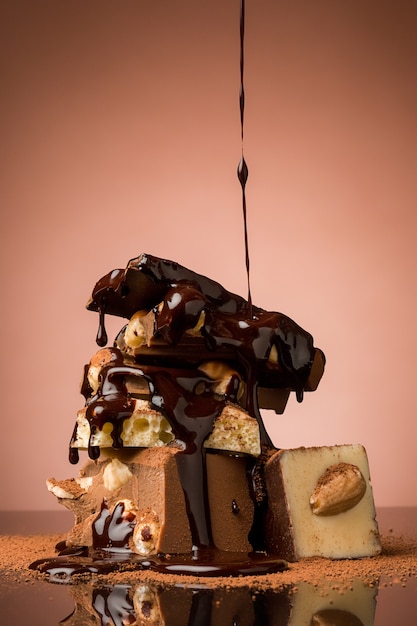 Free photo pile of broken chocolate on table against brown background and hot chocolate spray