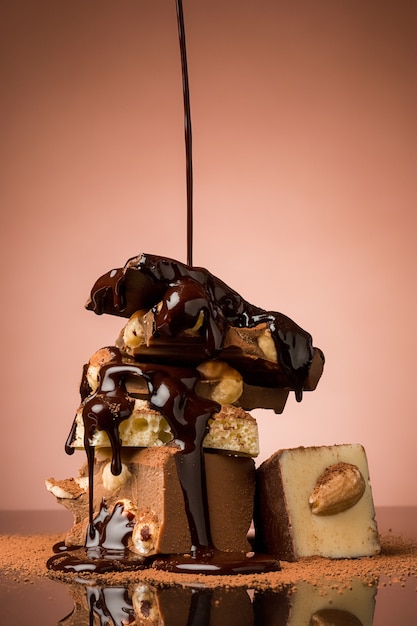 Free photo pile of broken chocolate on table against brown studio background and hot chocolate spray