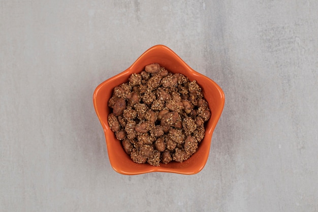 Pile of candies with sesame seeds in orange bowl.