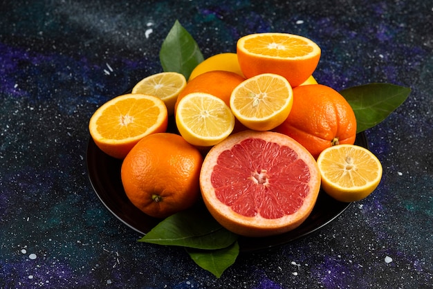 Pile of citrus fruits on black ceramic plate. 