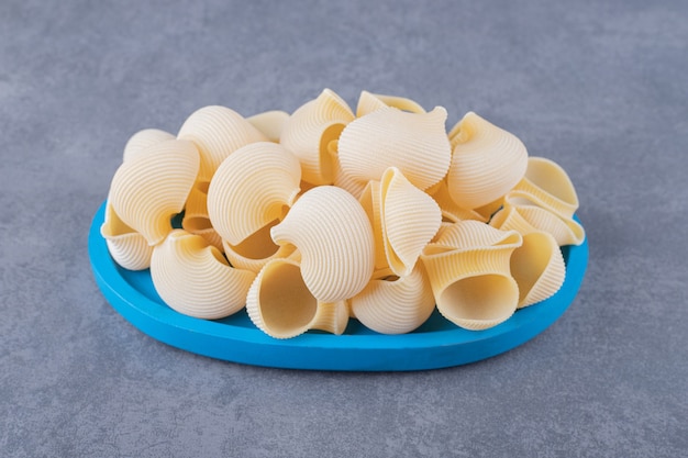 Pile of conchiglie pasta on blue plate.