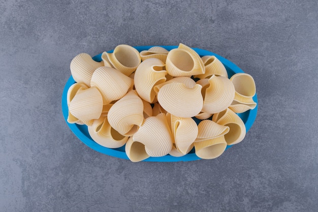 Pile of conchiglie pasta on blue plate.