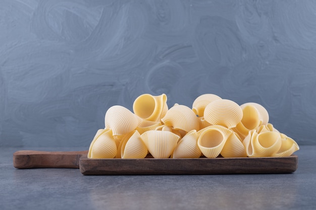 Pile of conchiglie pasta on wooden board.