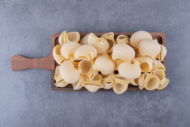 Pile of conchiglie pasta on wooden board.