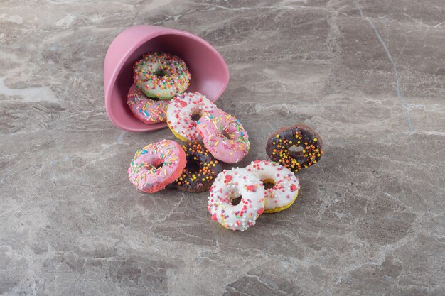 Pile of donuts and a fallen bowl on marble surface