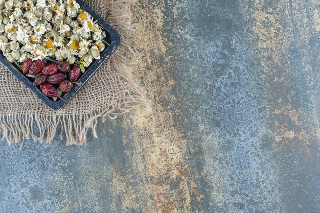 Pile of dried chamomile and rosehips on black board.