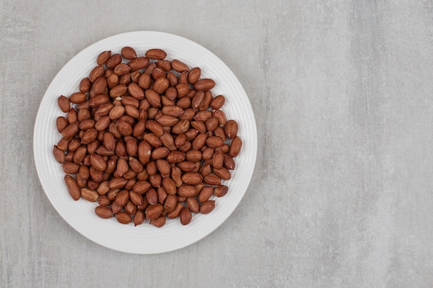 Pile of fresh peanuts on white plate.