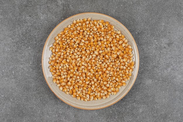 Pile of raw corn kernels on ceramic plate.